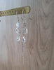 Long-length rhodium plated earrings with Swarovski crystal drops and swirl coins on display