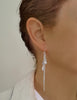 Woman wearing long-length rhodium plated earrings with Swarovski crystal drops and swirl coins