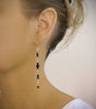 Woman wearing long-length 18K gold plated earrings with black Swarovski crystals