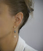 Woman wearing 18K gold plated hoop earrings with dark grey Austrian pearls and crystal drops.
