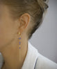 Woman wearing 18K gold plated long-length hoop earrings with Tanzanite Swarovski crystals.
