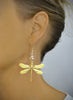 Woman wearing long-length 18K gold plated dragonfly statement earrings with Golden Shadow Swarovski crystals.