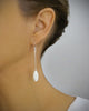 Woman wearing rhodium plated dangle earrings decorated with sparkling white Swarovski crystal pavé pendants.